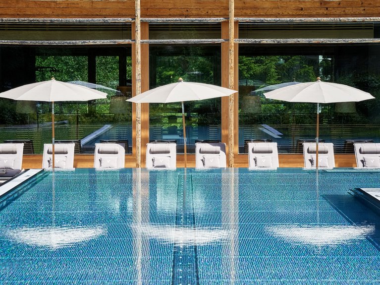 Swimmingpool mit weißen Sonnenschirmen und Liegestühlen vor Holzfenstern